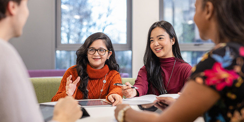 A group of four smiling students sitting working together around a table