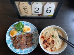 A board showing the date and two Chinese dishes on the table. One is beef and egg and the other is a bowl of noodles.