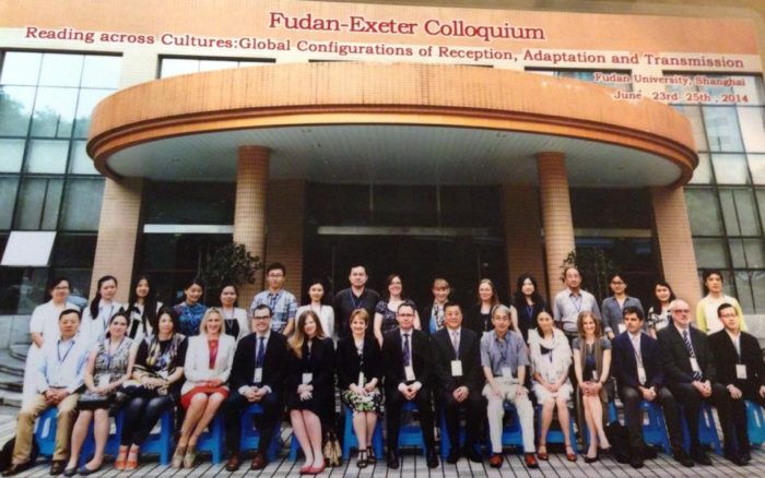 A group of professionals pose in rows in front of a large entrance and sign saying Fudan Exeter Colloquium