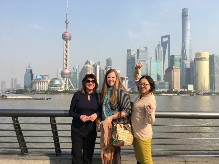 Three women smiling in front of the Shanghai skyline