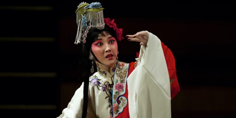A performer in traditional colourful Chinese dress and make up strikes a dramatic pose