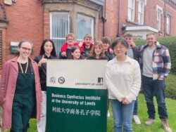 A group of Chinese and non-Chinese people gathered around a sign reading 'Business Confucius Institute at the University of Leeds' in English and Chinese