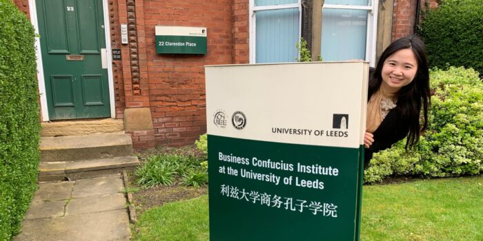 Chinese woman playfully looking out from behind the Business Confucius Institute sign outside the office.