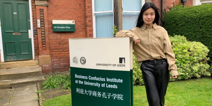 A Chinese woman standing by the Business Confucius Institute sign outside the office.