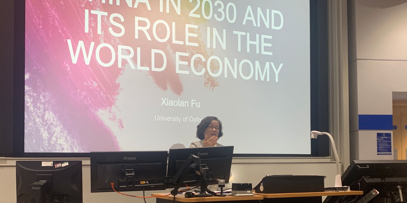 A woman standing behind a lectern. A title slide behind her reads Xiaolan Fu, University of Oxford.