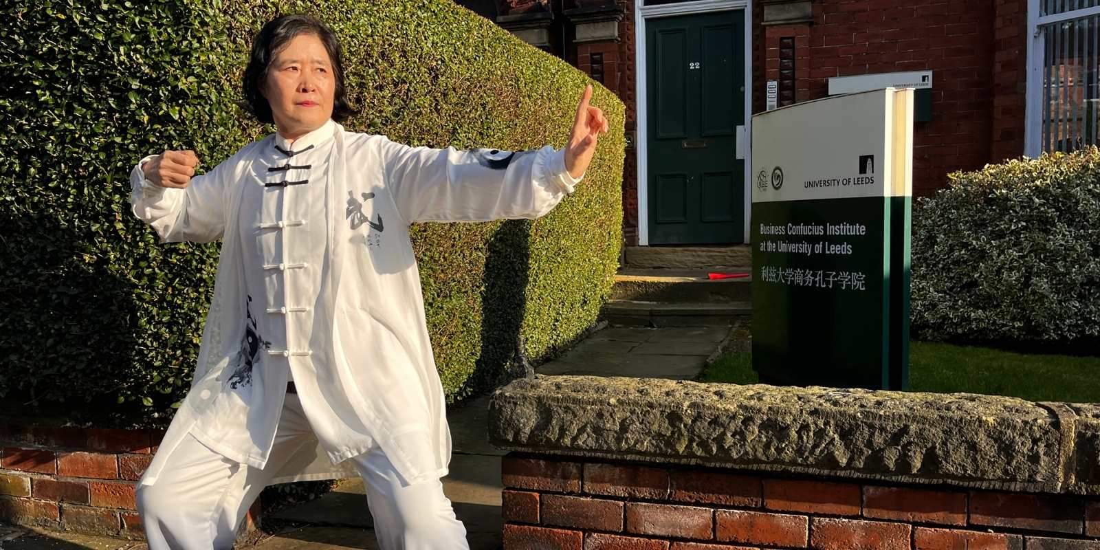 A Chinese woman in loose white martial arts clothing strikes a pose outside the Business Confucius Institute office
