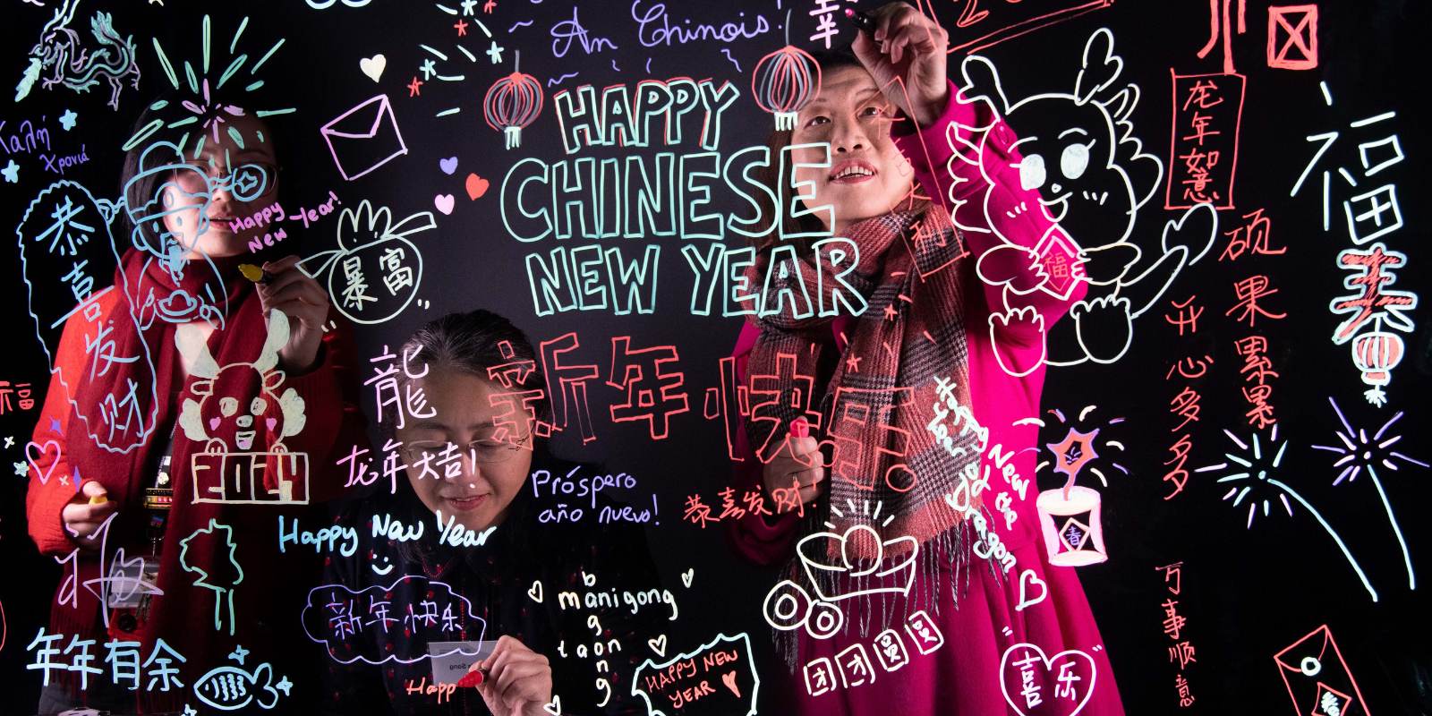 Three people add colourful messages to a glass board
