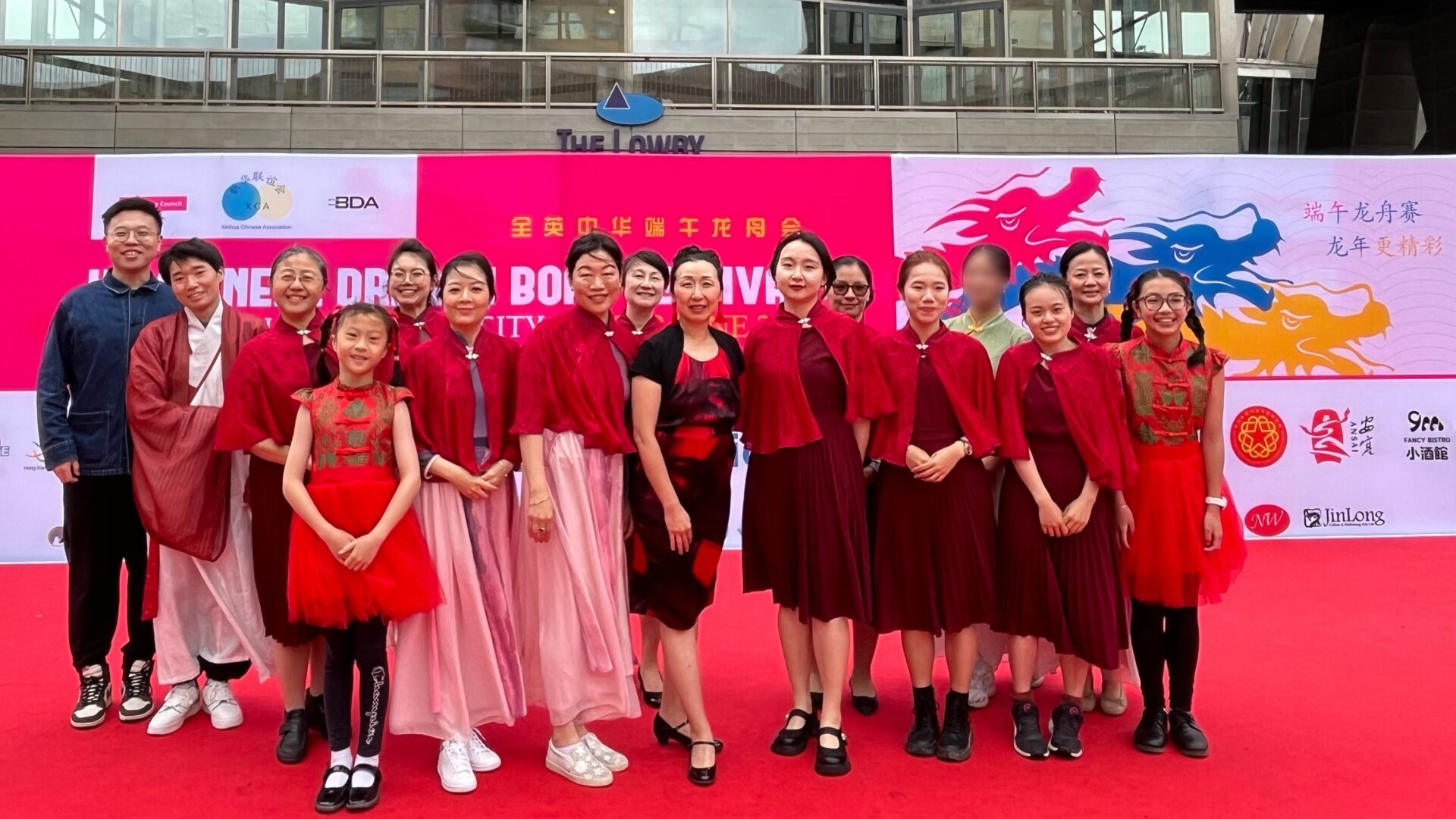 The performers are on stage, dressed in red and with the event signage behind them.